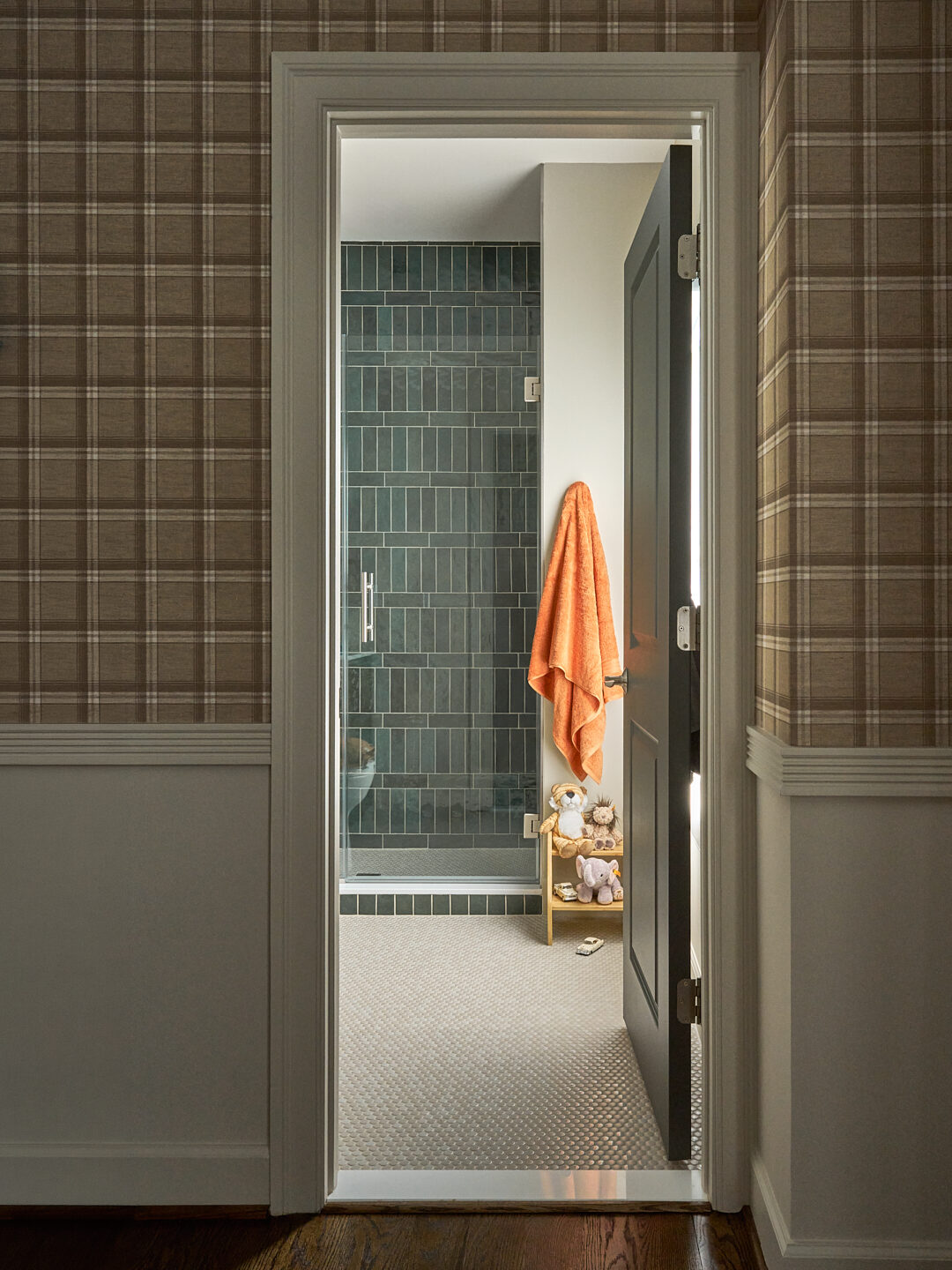 Millwood Road nursery bath doorway framed by plaid wallcovering with green tile shower